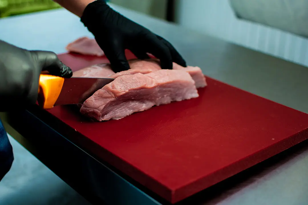 Carnicero profesional troceando carne sobre una tabla de corte industrial de polietileno P500 blanco.